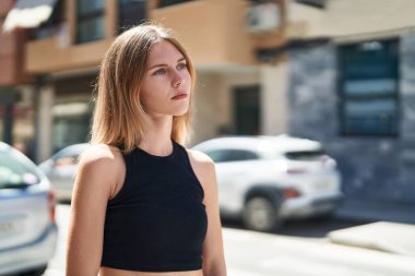 Sokakta ciddi bir ifadeyle yan tarafa bakan genç sarışın kadın.