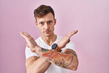 Pembe arka planda duran beyaz bir adam. Reddedilmiş yüz ifadesi. Kollarını kavuşturup negatif işaret veriyor. 