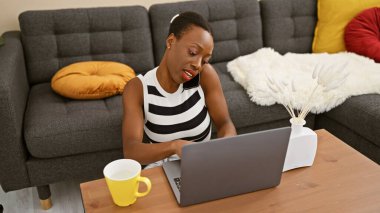 Güzel bir Afro-Amerikalı kadın ciddi bir online sohbete daldı. Evde dizüstü bilgisayar kullanırken telefonla konuştu. Kanepede oturdu, yanında kahve vardı.