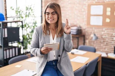 Ofiste çalışan genç İspanyol kadın gözlüklü, işaret parmağı takmış umut ve gözler kapalı bir şekilde gülümsüyor. Şans ve batıl inançlar. 
