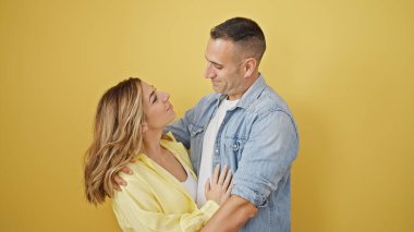 Sarı arka planda gülümseyen kadın ve erkek birbirlerine sarılıyorlar.