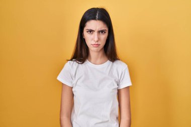 Sarı arka planda duran genç ve güzel bir kadın şüpheci ve gergin, sorun yüzünden surat asıyor. negatif kişi. 