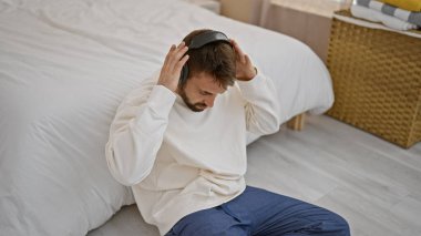 Genç İspanyol adam yatak odasında yerde oturmuş müzik dinliyor.