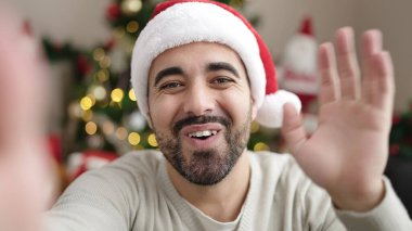 Evdeki Noel ağacının yanındaki koltukta oturan Latin asıllı genç adam.