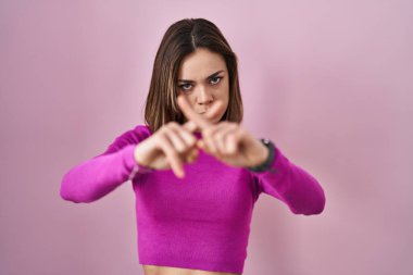 Hispanic woman standing over pink background rejection expression crossing fingers doing negative sign 