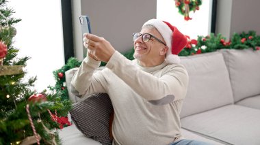 Orta yaşlı, kır saçlı bir adam evde Noel ağacına fotoğraf çeker.