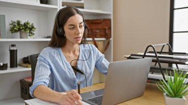 Genç, güzel bir İspanyol kadın işçi, işindeki başarısına dalmış, kulaklıkları laptopla birleştirmiş, evde rahat profesyonellik yayıyor..