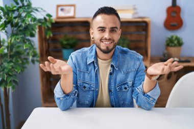 Young hispanic man sitting on table speaking at home
