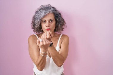 Pembe arka planda gri saçlı orta yaşlı bir kadın yumruğunu savuşturmaya hazır kızgın ve üzgün bir yüz, problemden korkuyor. 