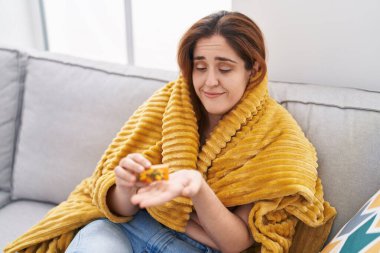 Battaniyeyle kaplanmış, evde hap alan genç bir kadın.