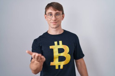 Beyaz, sarışın, bitcoin tişört giyen neşeli gülümseyen, yardım eli uzatan ve kabul gören bir adam.. 