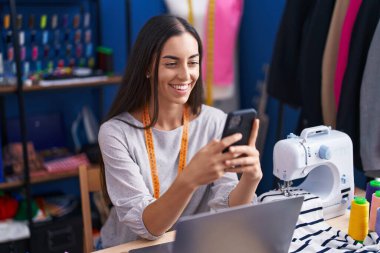 Güzel İspanyol kadın terzi elbise fabrikasında akıllı telefon ve laptop kullanıyor.