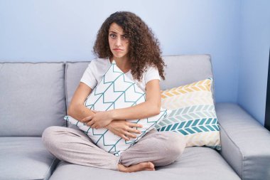 Evdeki koltukta oturan kıvırcık saçlı, kuşkucu ve gergin İspanyol kadın sorun yüzünden kaşlarını çatıyor. negatif kişi. 