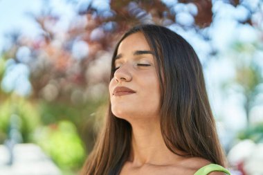 Young beautiful hispanic woman breathing with closed eyes at park
