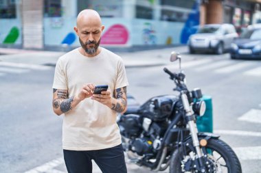 Genç kel adam akıllı telefon kullanıyor ve sokakta ciddi bir yüz ifadesi var.