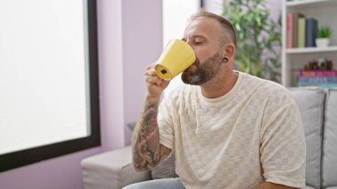 Derin düşüncelere dalmış yakışıklı genç adam, rahat bir şekilde evde oturuyor, rahatlatıcı bir sabah kahvesini yudumluyor..