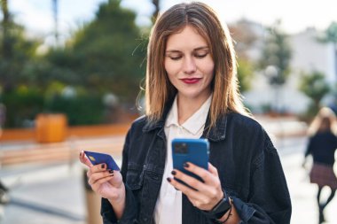 Genç sarışın kadın parkta akıllı telefon ve kredi kartıyla alışveriş yapıyor.