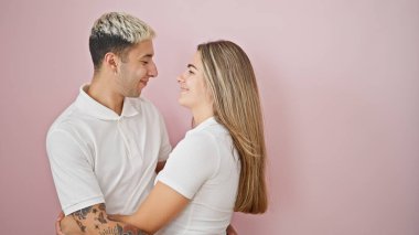 Güzel bir çift gülümsüyor. Birbirlerine sarılıyorlar ve soyutlanmış pembe arka plana bakıyorlar.