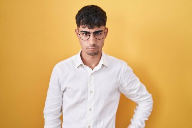 Sarı arka planda duran Latin asıllı genç adam şüpheci ve gergin, sorun yüzünden surat asıyor. negatif kişi. 