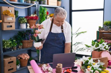 Çiçekçide dizüstü bilgisayar kullanan kır saçlı bir çiçekçi.