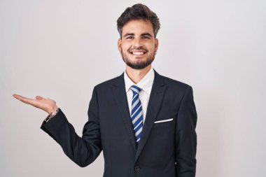 Dövmeli, takım elbiseli, kravatlı, neşeli gülümseyen, eli avucunda kameraya bakan genç İspanyol bir adam.. 