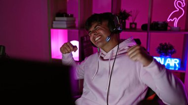 Young hispanic man streamer playing video game dancing at gaming room