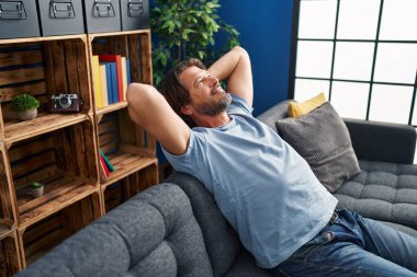 Middle age man relaxed with hands on head sitting on sofa at home