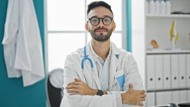 Kollarını kavuşturup klinikte gülümseyen genç İspanyol doktor.