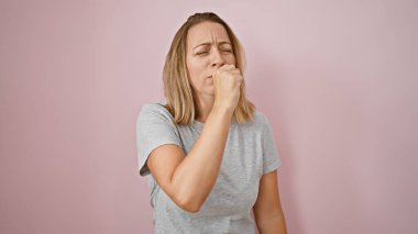 Üşüttün mü? Güzel, genç, sarışın bir kadın öksürüyor. İzole edilmiş pembe bir arka planda grip benzeri belirtiler gösteriyor. Soğuk ama ciddi bir ifade. Covid-19 'un artan endişesi..