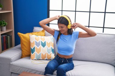 Genç ve güzel İspanyol kadın dans ediyor ve müzik dinliyor. Evdeki koltukta oturuyor.