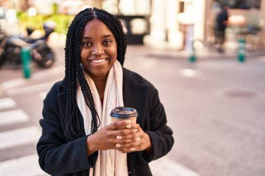 Afro-Amerikalı kadın gülerek sokakta kahve içiyor.
