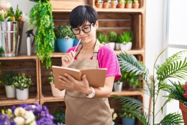 Çiçekçide çiçekçi, orta yaşlı Çinli kadın şüpheli bir ifadeyle defter okuyor.