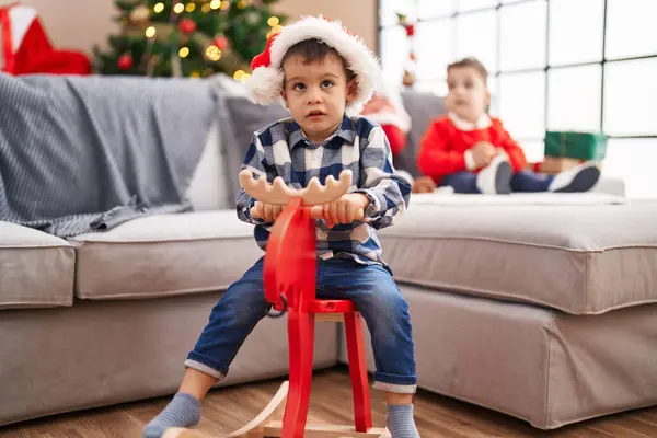 自宅でクリスマスツリーでロッキングトナカイと遊ぶ2人の子供 — ストック写真
