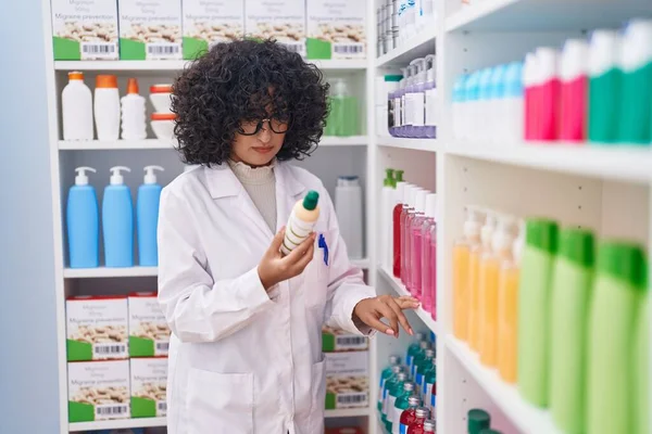 Young middle eastern woman pharmacist holding shampoo bottle at pharmacy