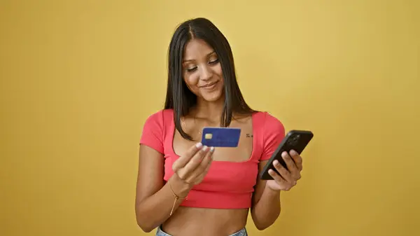 年轻的拉丁女人用智能手机和信用卡在孤立的黄色背景下购物 — 图库照片