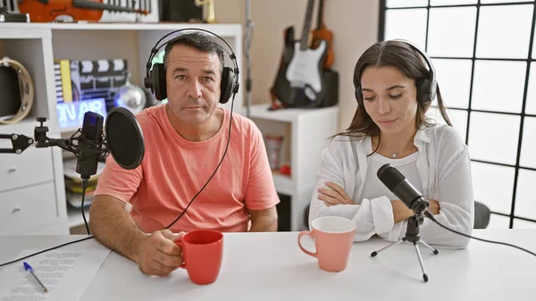 Man and woman interviewers sharing a coffee moment in a radio studio