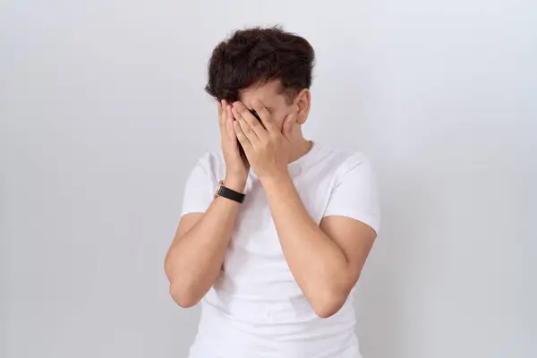泣きながら手で顔を覆う悲しい表情のカジュアルな白いTシャツを着ている若い非バイナリ男性 うつ病コンセプト — ストック写真