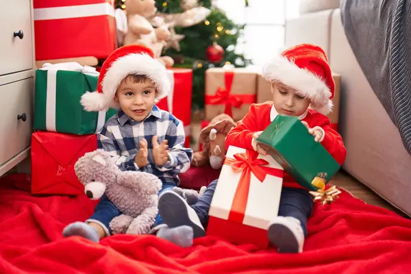 两个小孩拿着礼物和玩具熊坐在家里的圣诞树旁 — 图库照片