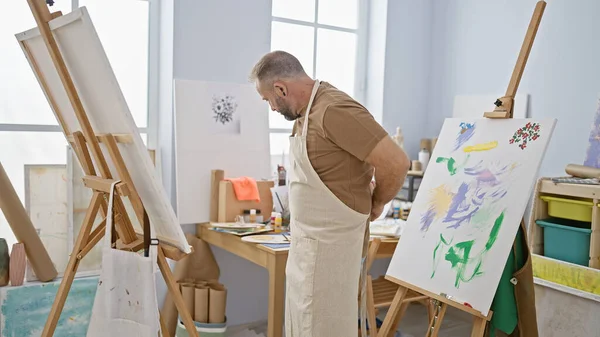 轻松的年轻画家在绘画时专心致志地集中精神 穿着围裙站在他的艺术大学工作室里 四周都是绘画 画笔和帆布 — 图库照片