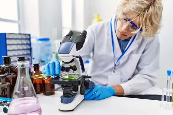 stock image Young blond man scientist using microscope pouring liquid on sample at laboratory