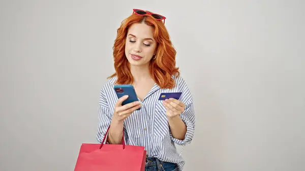 スマートフォンやクレジットカードを利用した若い赤毛の女性は 隔離された白い背景の上にショッピングバッグを保持 — ストック写真