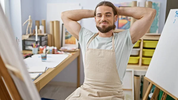 Young hispanic man artist smiling confident relaxed with hands on head at art studio