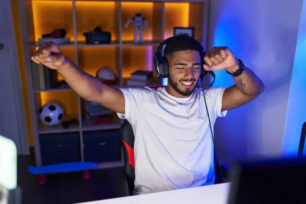 Young latin man streamer playing video game with winner expression at gaming room