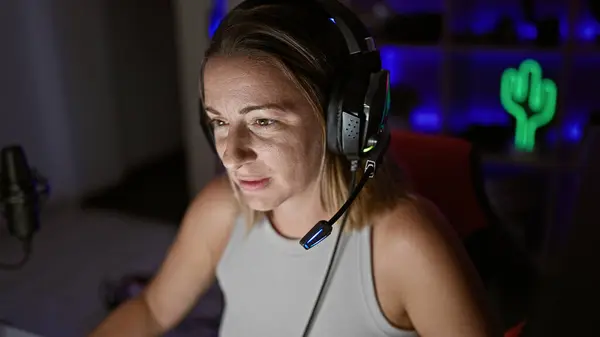 魅力的な若いブロンドの女性ストリーマーは 彼女のゲームルームに閉じ込められ 夜に彼女のコンピュータ上でライブストリーミングビデオゲームをプレイしながら 未来的な技術を使用して 焦点と深刻な — ストック写真