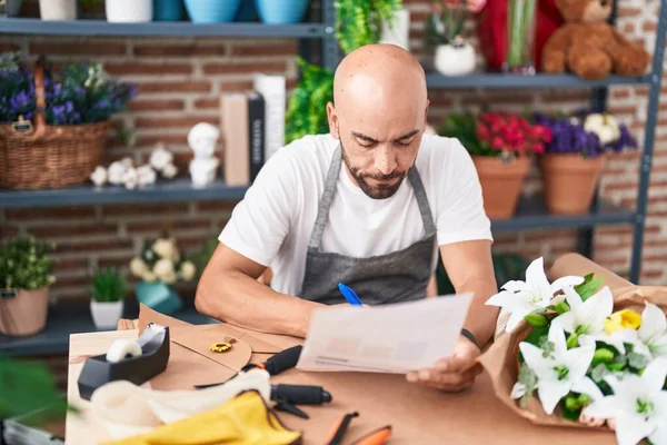 Young bald man florist writing on document at florist