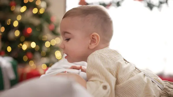 Adorable toddler sitting on sofa by christmas tree with serious expression at home