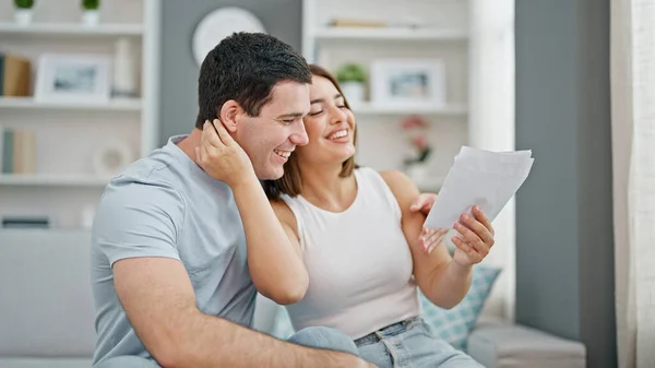 Beautiful couple reading document sitting on sofa smiling at home