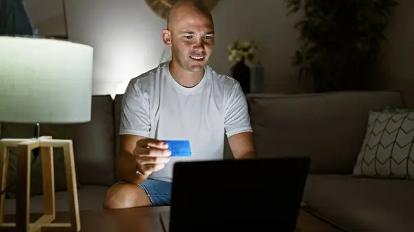 Young hispanic man shopping with laptop and credit card sitting on sofa at home