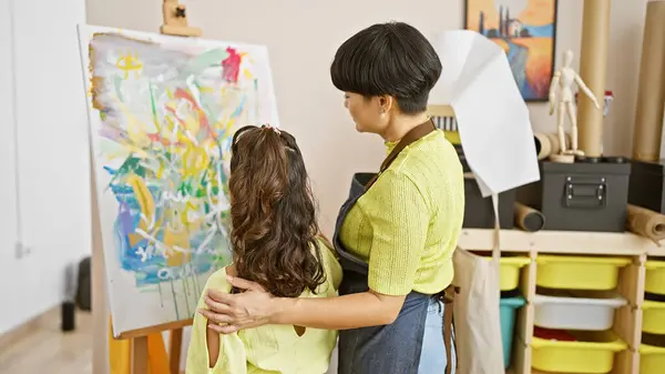 Art class emotion, student and artist teacher share an inspiring hug, looking along a drawing in art studio together