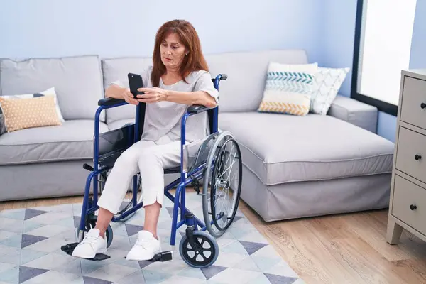 Evde Tekerlekli Sandalyede Oturan Orta Yaşlı Bir Kadın Akıllı Telefon — Stok fotoğraf